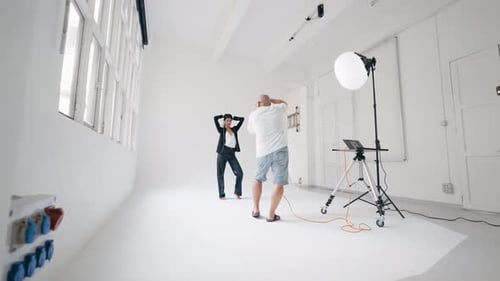 Photographe professionnel guidant un modèle posant dans un studio blanc
