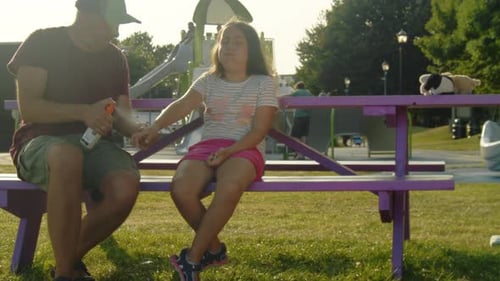 Father Spraying Mosquito Repellent on Daughter at Sunset Playground