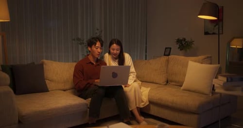 Young Couple Uses Laptop on Couch at Night