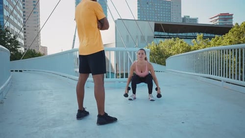 Woman Doing Squats with Weights, Man Watching