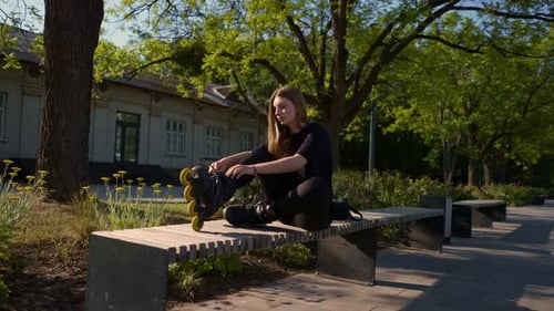 young beautiful girl in park tying laces on roller skates before skating workout active lifestyle