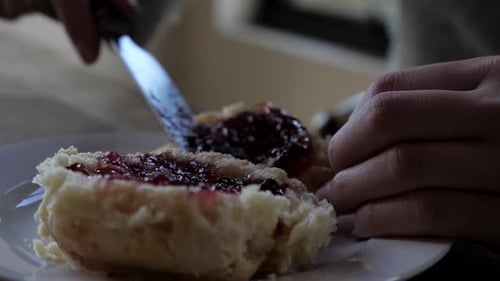 Une femme répand à la main de la confiture de fraises et de framboises d'un scone traditionnel fraîchement sorti du four à l'autre et
