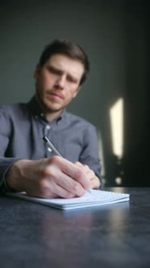 Man Writing in Notebook at Table Indoors