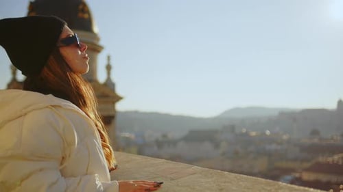 Chica en una azotea mirando una ciudad con gafas de sol al atardecer