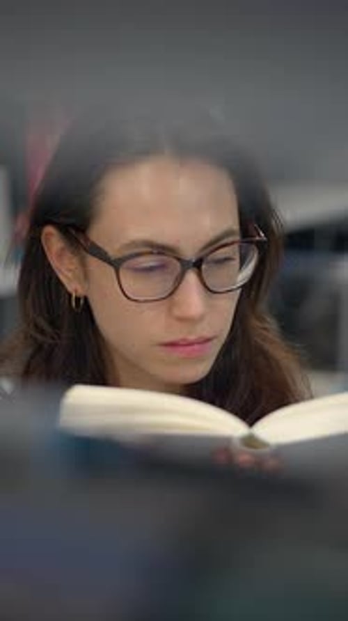 A Young Woman is Deeply Engaged in Reading a Book Within a Calm Modern Library Setting