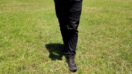A man with black trouser and black shoe walking in the field.