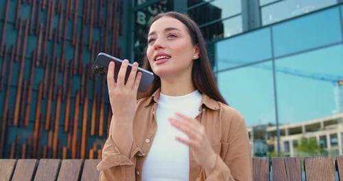 Brunette Woman Uses Voice Assistant on Smartphone Outdoors