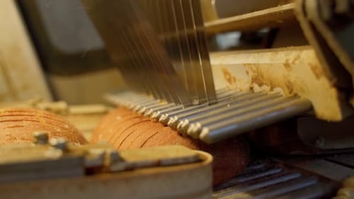 Professional bread cutting mechanism inside long loaf slicer on factory indoors close up