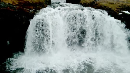 A close-up view of a waterfall in Iceland's mountains, resembling a flowing curtain, is captured as