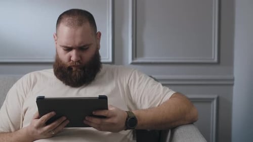 Man Sits in Chair Using Tablet