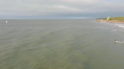 Establishing aerial view of a group of people engaged in kitesurfing, overcast winter day, high wave