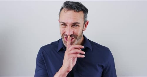 Secret, gossip and finger on lips of man in studio with privacy, quiet or confidential news on grey