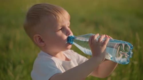 Little Kid Drinking Water From a Bottle in a Grassy Field