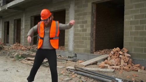Belo construtor de colete e capacete, dançando engraçado no canteiro de obras, trabalhador da construção civil dançando
