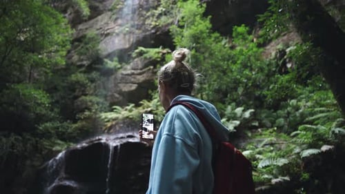 Woman Photographs Waterfall in Forest with Smartphone