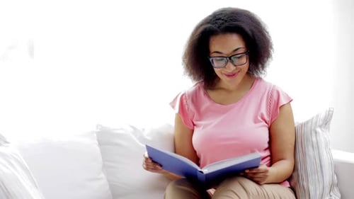 Leisure, Literature And People Concept - Smiling African American Young Woman In Eyeglasses Readi...