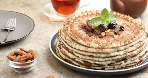 Leckerer Crêpe-Kuchen mit Nüssen, Schokolade und Kakaopulver, serviert auf einem hellen Tisch, rotierend