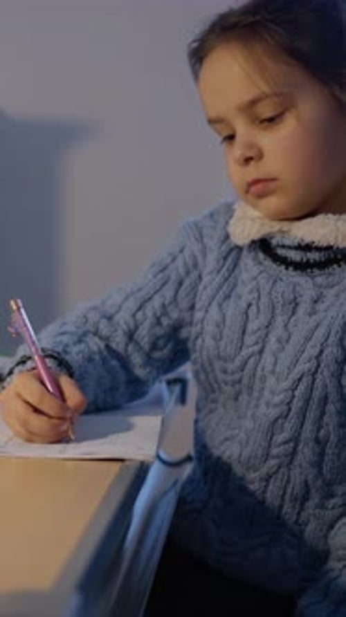 A Young Girl is Thoughtfully Studying and Writing Diligently at a Desk in a Cozy Warm Home
