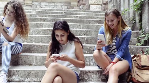Trendy teenage students with gadgets studying together outside university building