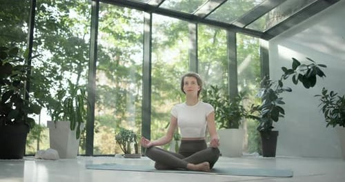 Young Caucasian Fitness Woman Sitting in Lotus Position on a Yoga Mat in a Modern Studio with Plants