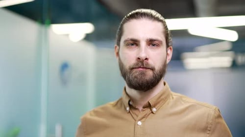 Portrait of serious bearded businessman standing at workplace in modern business office. Head shot