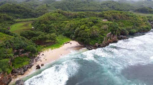 Vue aérienne des vagues de calotte blanche s'écrasant sur une plage tropicale et des falaises côtières, Indonésie