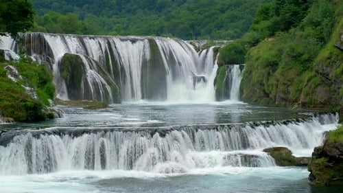Wasserfälle, die Felsen herunterstürzen, schaffen eine natürliche Szene mit fließendem Wasser. Grüne Bäume befinden sich in der