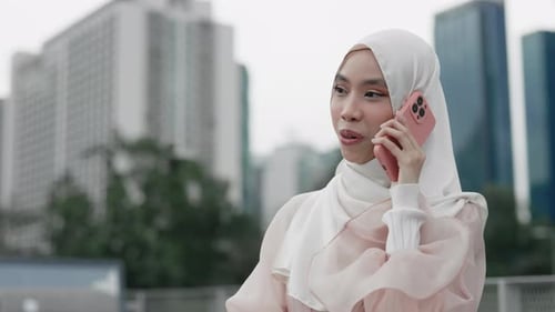 Elegante señora sonriente que lleva el hijab afuera participa en una llamada telefónica con sus amigos