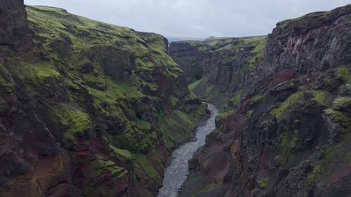 High-angle view tracking a narrow river carving through ancient volcanic cliffs.