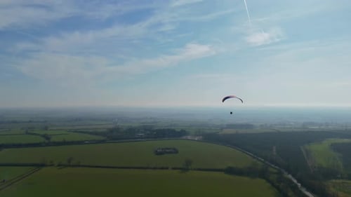 Aerial video high above the village as a paraglider soars peacefully across a wide open sky.