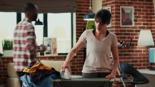 Woman Ironing Clothes While Man Works in Background