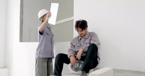 Asian female engineer standing with blueprint instructs seated male worker during professional