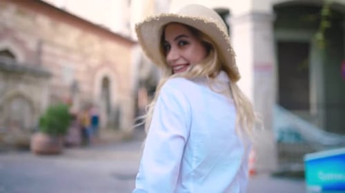 Attractive young beautiful girl with hat walks and discovers places in narrow street