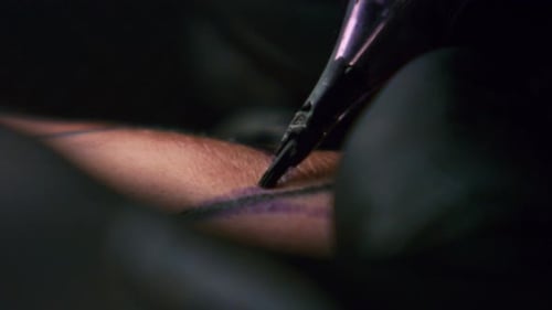 Der Tätowierer aus nächster Nähe zeigt, wie man ein schwarzes Tattoo mit Farbe auf der Rückseite eines Clies bekommt