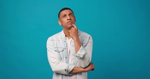 Young African American Man Thinking and Looking Up Standing on Blue Studio Background