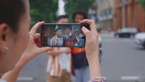 Woman Holding Smartphone to Take Photo of Her Friends Walking in City