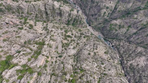 Aerial View of a Rugged Rocky Canyon with Sparse Vegetation and a Narrow River Running Through It