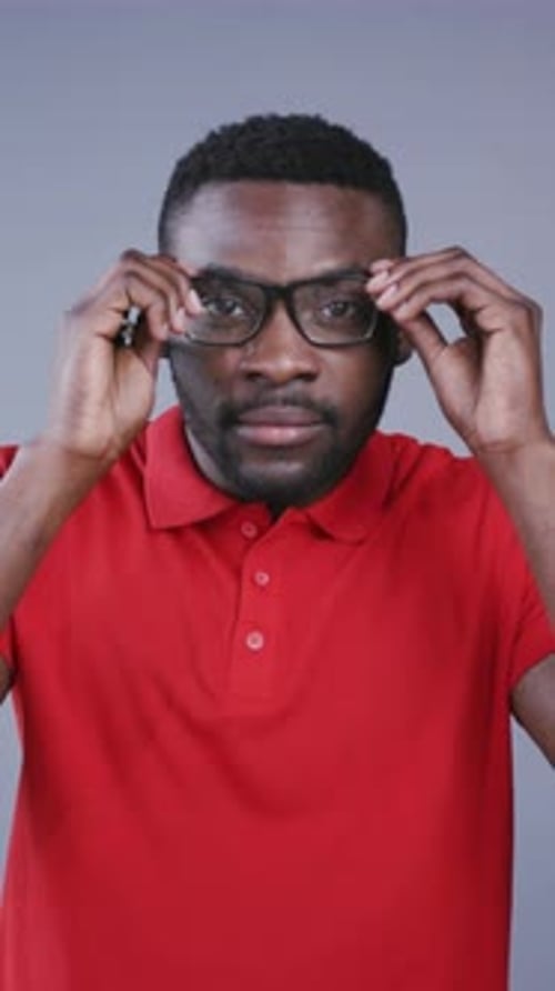 Nahaufnahme eines attraktiven afroamerikanischen Mannes, der eine nerdige Brille aufsetzt und charmant lächelt