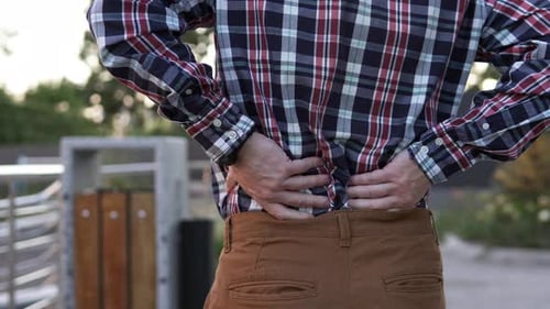 A man feels a sharp pain in his lower back and massages his back during a break.
