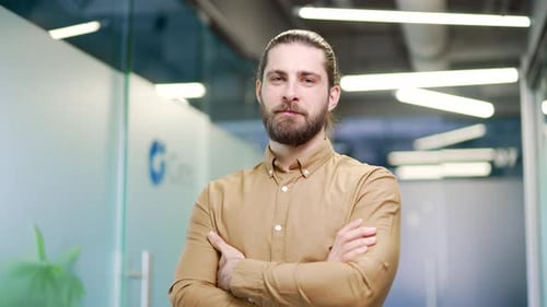 Portrait of smiling bearded businessman standing with crossed arms at workplace in a business office