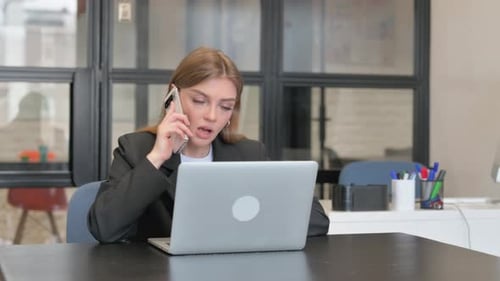 Young Woman Talking on Phone while Using Laptop