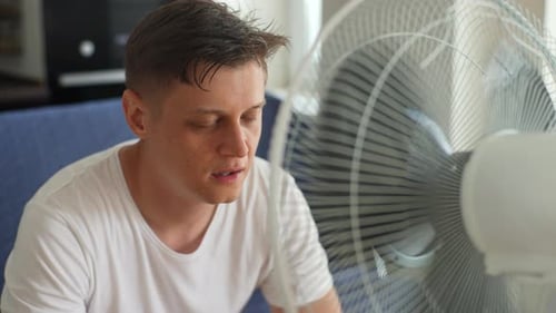 Overheated Exhausted Young Man Suffering From Heat High Temperature at Home Sitting on Sofa in Front