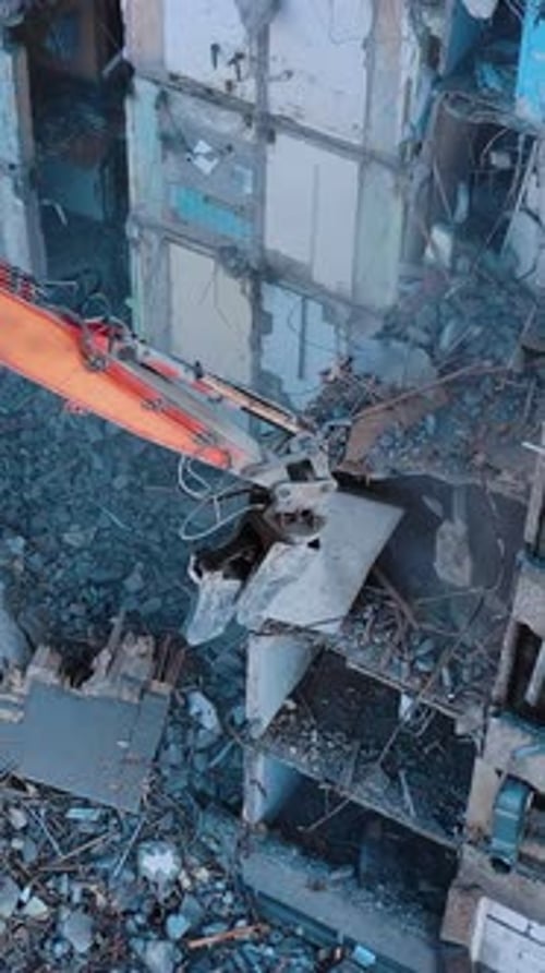Excavator crashing floors of an old building and dusty debris falling down.