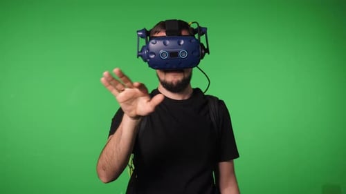 A Man Uses Virtual Reality Glasses to Play in a Studio on a Green Background