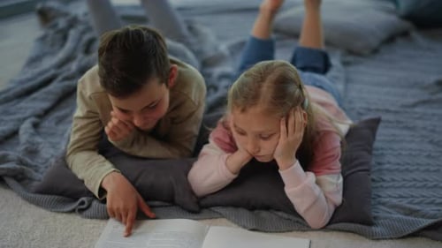 Brother and sister enjoying reading book pages together indoors at home