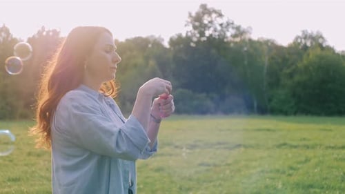 Woman Blowing Bubbles in a Field at Sunset