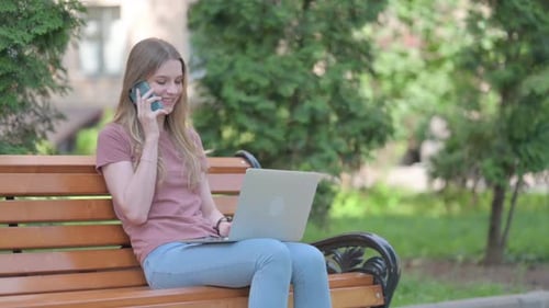 Woman Sits on Park Bench with Laptop and Phone