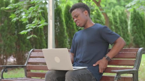 Casual African Man with Back Pain While Using Laptop in Park