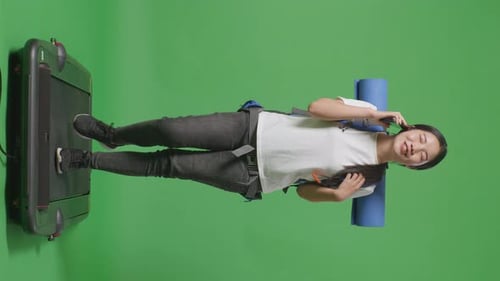 Full Body Of Asian Female Hiker Talking On Smartphone While Walking On A Treadmill On Green Screen