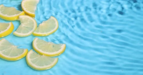 Fresh Lemon Slices Floating On Blue Water Surface